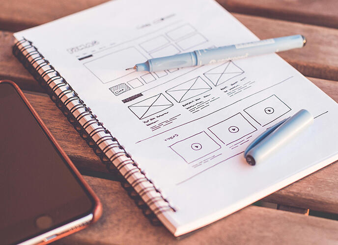 Notebook and Mobile Phone Image On a wooden table, a notebook, pen, and smartphone are placed, illustrating a casual work or study scene.